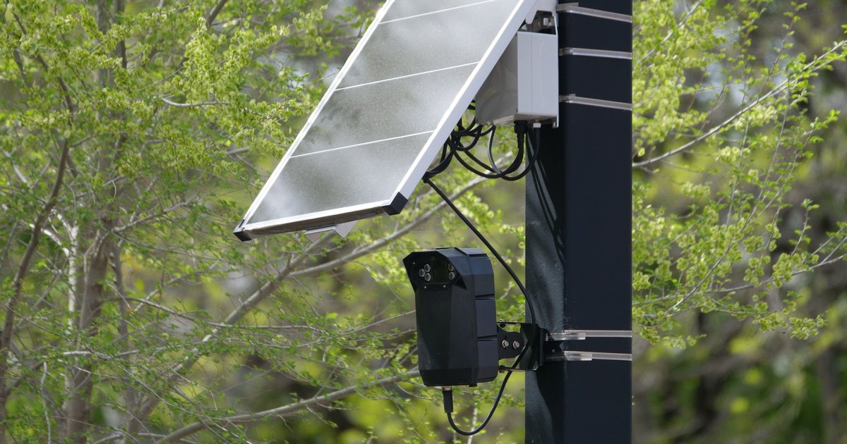 Pole-mounted automatic license plate reader camera scanning passing vehicles at a neighborhood intersection
