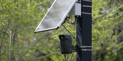 Pole-mounted automatic license plate reader camera scanning passing vehicles at a neighborhood intersection