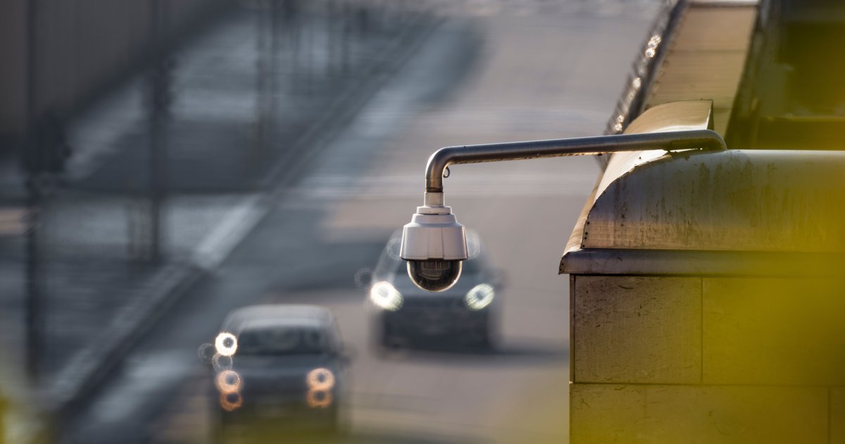 Automatic license plate readers (ALPRs) mounted on a pole scanning passing cars on a city street at dusk