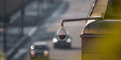 Automatic license plate readers (ALPRs) mounted on a pole scanning passing cars on a city street at dusk