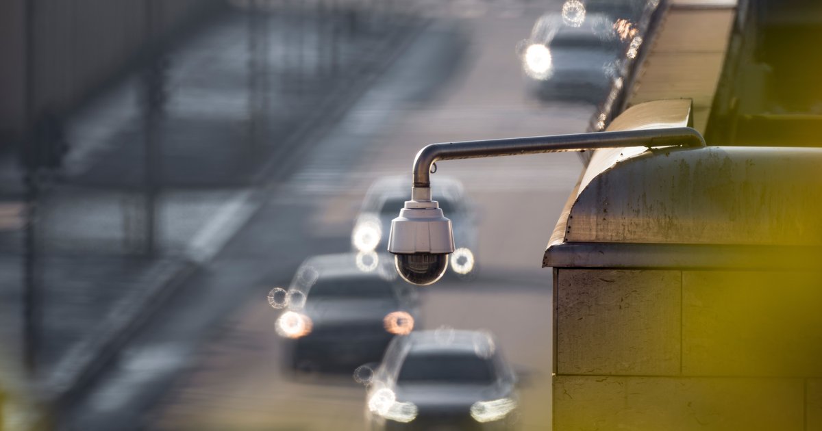 Automatic license plate reader camera mounted on a pole along a Massachusetts road at dusk.