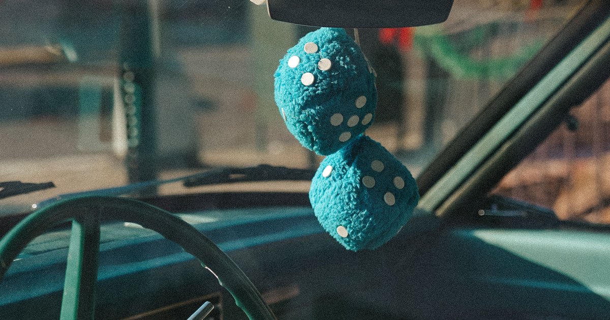 Red fuzzy dice hanging from a classic car rearview mirror showing the traditional fuzzy dice meaning