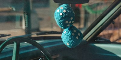 Red fuzzy dice hanging from a classic car rearview mirror showing the traditional fuzzy dice meaning