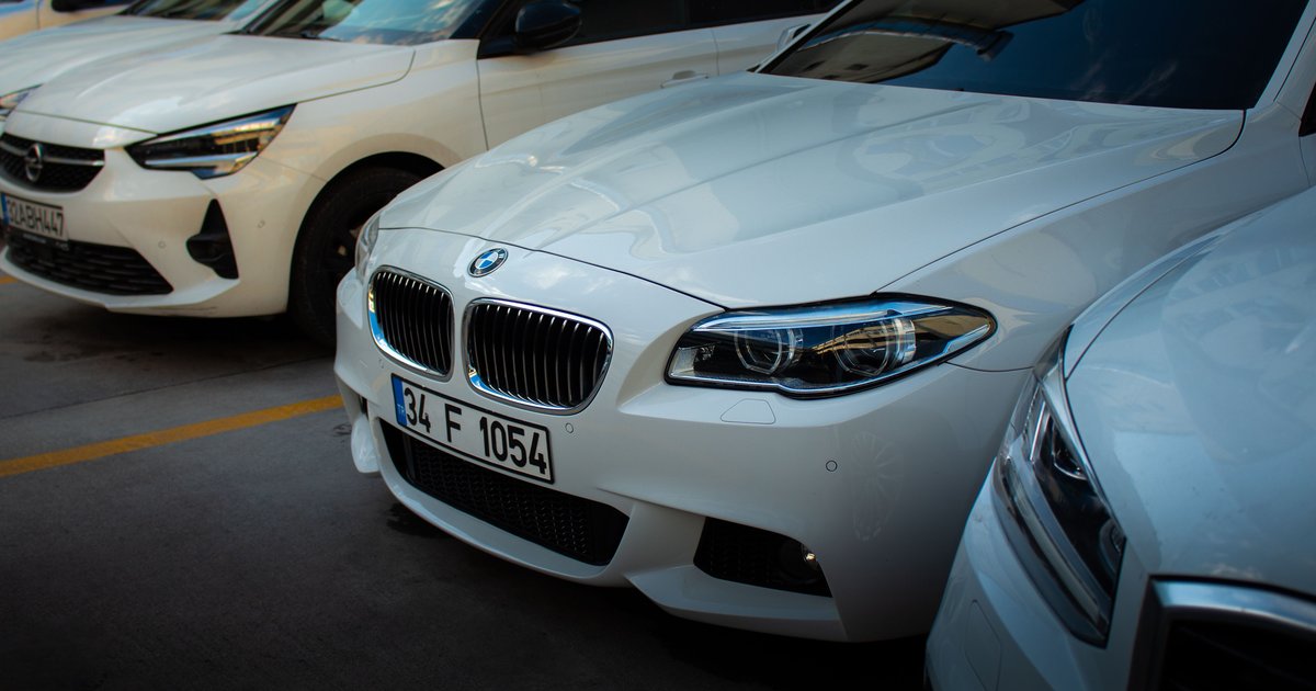 Person holding a smartphone next to a parked car checking how to contact the car owner by number plate