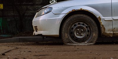 Dusty abandoned vehicle with flat tire parked on a San Jose residential street awaiting report and removal.