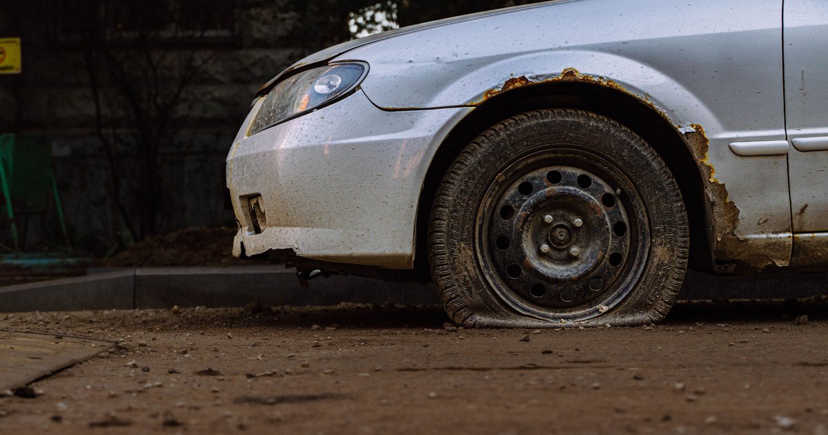 Dusty abandoned vehicle with flat tire parked on a San Jose residential street awaiting report and removal.