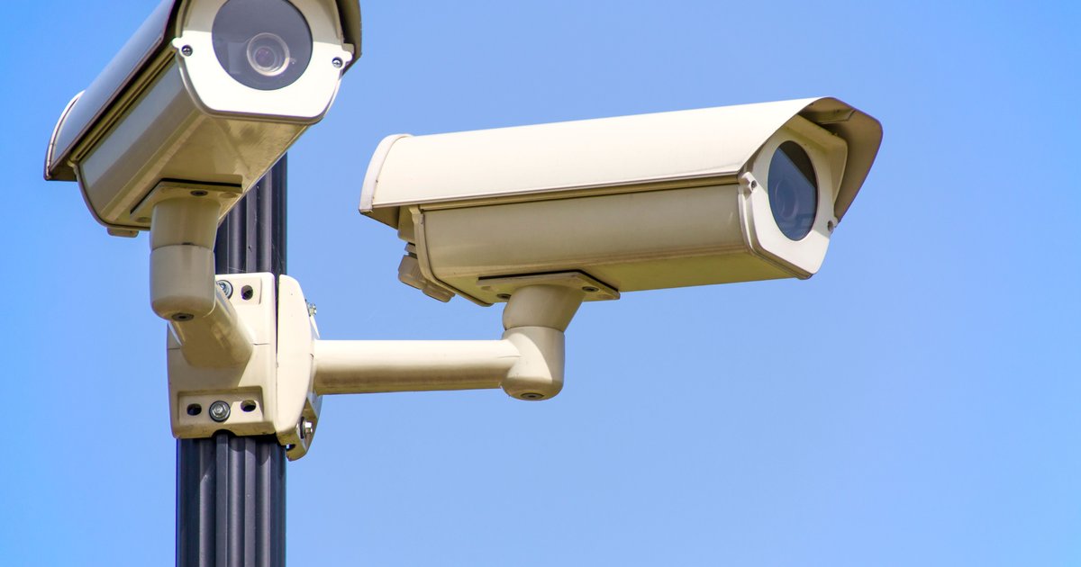 A pole-mounted automated license plate reader camera scanning passing traffic on a suburban road at dusk.