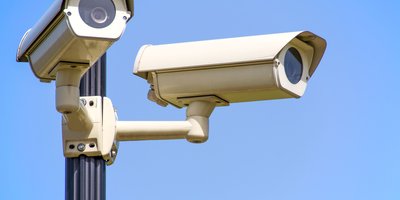 A pole-mounted automated license plate reader camera scanning passing traffic on a suburban road at dusk.